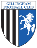 A shield with the words "Gillingham Football Club" in the top portion and the remainder divided into two sections, the left containing black and white vertical stripes and the right a depiction of a white horse rearing up on its hind legs on a blue background