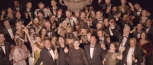 Lorde and other guests dressed in formal clothing at a cocktail party as they smile to a camera