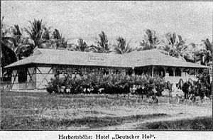 A small single story building, with grass roof and veranda, next to bushes