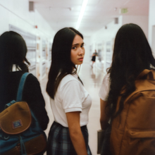 Niki dressed as a high school student, walking on her school's hallway with two of her classmates.