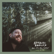 The cover consists of a smiling bearded man against a forest backdrop, with a ray of sunlight showing on the right. The artist's name and album title appear on the bottom right corner, colored in white.