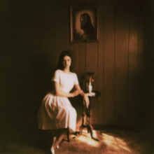 Cain poses for a picture, seated in a white dress beneath a picture of Jesus Christ.