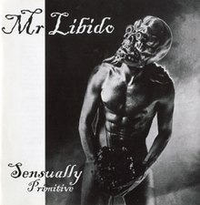 In a dark room stands a muscular naked man. In his hands, which are placed in front of his crotch, he is holding a bunch of flowers. Over his head he is wearing a skull like rubber mask. In the upper left corner is written Mr Libido, and in the lower left is written Sensually Primitive.