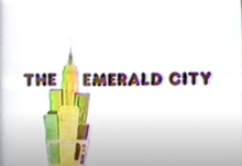 Title card for The Emerald City showing a stylized Manhattan skyline emerging from inside a television box, next to the name of the show