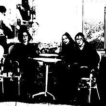 A very grainy black and white photo of the band seated at a table