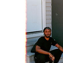JPEGMAFIA sitting on a porch in front of a house with grey walls and a white door, he is holding a drink and his eyes are closed. Half of the photo is completely white due to a first of the (film) roll burn effect