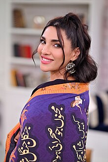 Zhalay Sarhadi wearing a purple quilt with Arabic writing, head turned to look directly at camera