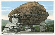 and old postcard of a boulder with a band around it on three small piers of smaller rocks.