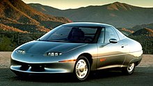 Picture of a unusally-shaped concept car, taken in a mountainous environment with the sun setting.