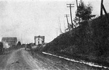 A black and white photo showing a gravel road curves around a hill