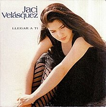 Image of Jaci Velasquez wearing a black dress sitting down and facing the sand.