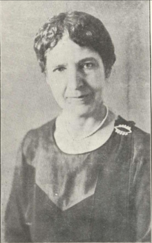 A black and white photo of a white woman with short dark hair, 54 years old, wearing a pearl necklace.