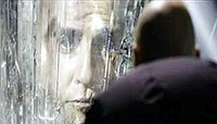 Лицо мужчины появляется в кристаллической стене, в то время как лысый мужчина, спиной к камере, смотрит на него.