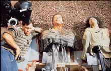 A photograph of animatronics of Arnold Schwarzenegger and Rachel Tictoin, built from the chest upwards, lying down next to a crew member