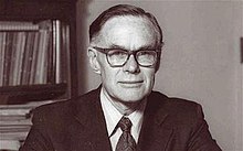 Black and white portrait photograph of John Forfar, in an office, wearing a jacket, shirt, tie and glasses.