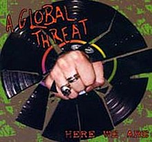 A fist with rings on its middle and ring fingers punches through a vinyl record. In red in the top left corner is "A Global Threat;" at the bottom right, "Here We Are."