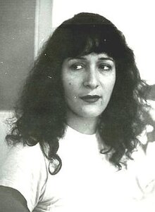Black-and-white upper-body photo of Israeli poet Miri Ben-Simhon. She is wearing a white t-shirt, has wavy dark hair past her shoulders, and is looking to the left of the camera.