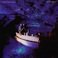 An album cover showing four men in a rowing boat inside a blue lit sea cave. Two men are stood side-by-side at the back of the boat each holding an oar, the third man is sat in the centre of the boat and the fourth is leaning over the front of the boat with his hand in the water. The band's name is in the top-left of the cover and the album's name is in the top-right, both in white text.
