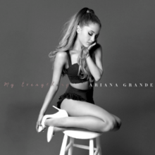 Ariana Grande kneeling on a stool, with her head resting on her hand