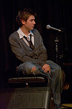 A man sits on a stool next to a microphone