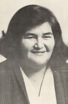 Portrait of a woman with shoulder-length dark hair, wearing a white v-necked blouse under a dark sweater jacket