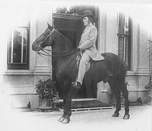 Black and white photograph of Hill riding his horse in front of Langford House.
