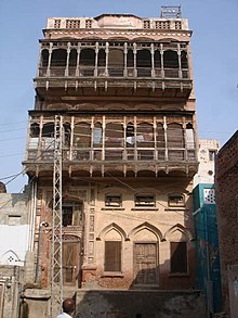 Reddish, three-story residential building with balconies on the top two stories.