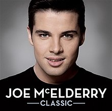 A close-up of McElderry wearing a black t-shirt against a grey background. Both the artist's name and album title appear below him, colored in white.