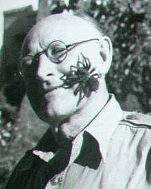 A smiling man with a large spider on his cheek