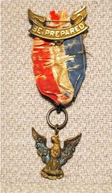 An old Eagle Scout medal, the pendant is an eagle with wings spread suspended from a red, white and blue ribbon attached to a scroll bar with the words Be Prepared