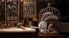 Film screenshot of a rabbit in a cage desperately reaching for a carrot sitting on a nearby table. The table has various jars on it, and posters for the magic show can be seen on the wall in the background.