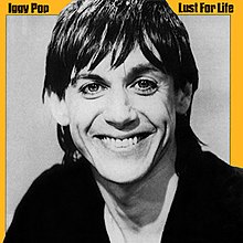 A middle-aged man with long black hair grinning at the camera, with a yellow border. The words "Iggy Pop" appear in the top left corner; the words "Lust for Life" appear in the top right.