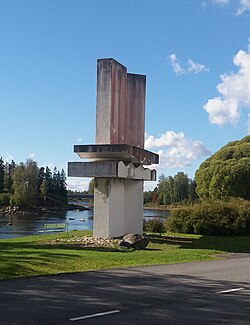 Suurikokoinen, betonista tehty veistos joen rannalla.