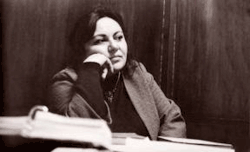 צילום שחור-לבן של ארפניק צ'ארנץ. היא ישובה מאחורי שולחן מכוסה בניירות וספרים, ומשעינה את לחייה על ידה.