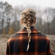 Foto punggung Swift. Dia menggunakan mantel kotak-kotak dengan rambut dikepang. Latarnya adalah gambar kabur dari sebuah hutan.