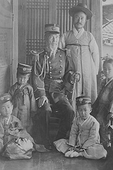 Juns Čhiho stāv aizmugurē. Viņa tēvs, Juns Ungs-nyeol ir apsēdies, apģērbies Korejas Impērijas rietumu formā. Fotogrāfija attēlo ģenerāli ar savu ģimeni. 1910. gadā.