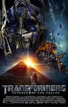 The human-like faces of two robots stand atop a pyramid. A helicopter flies over an industrial facility on the right side of the image, and a young couple is seen in front of the pyramid. The film title and credits are on the bottom of the poster.