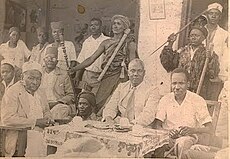 Sheikh Suleiman Takadir, Mbutta Milando, John Rupia na Julius Nyerere. Waliowazunguka na silaha za jadi ni Bantu Group, kundi la vijana wa TANU lililokuwa linatoa ulinzi kwa viongozi wa TANU. Picha hii ilipigwa mwaka wa 1955.