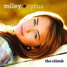 A female teenager lies on her back with her head is tilted over bannwkdnnwqdjlqnd llneln2lThe teen wears a plaid shirt, pink lipstick, and has blue green eyes. The words "Miley" and Cyrus", separated by a blue star, are printed in white above her face, and the words "the climb" are printed below her face.