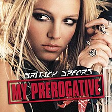 The face of a blonde woman. She is holding a microphone in her hand next to her head, while looking towards the left side of the picture. She is wearing different rings in her fingers. She is wearing a black vest. On the lower part of the image, the words "My Prerogative" are written in red capital letters inside a box of the same color.