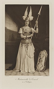 Black-and-white photograph of a standing young woman dressed in armor with a helmet and spear