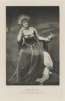 Black-and-white photograph of a seated woman richly dressed in a dress with symbols of the night sky
