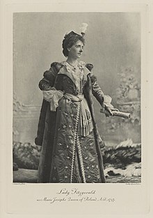 Black-and-white photograph of a standing woman richly dressed in an historical costume