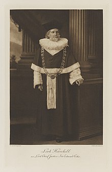 Black-and-white photograph of a standing man richly dressed in an historical costume wearing a very large ruff around his neck, fur on his robe and sleeves, and the insignia of an honor