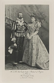 Black-and-white photograph of a standing man and woman richly dressed in historical costumes