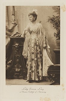 Black-and-white photograph of a standing woman richly dressed in an allegorical costume with stars on the dress