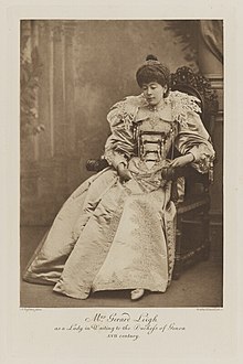 Black-and-white photograph of a seated woman richly dressed in an historical costume