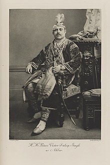 Black-and-white photograph of a seated man richly dressed in a costume