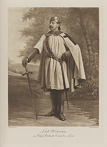 Black-and-white photograph of a standing man richly dressed in an historical costume with a helmet and sword