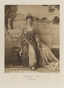Black-and-white photograph of a seated woman richly dressed in an historical costume